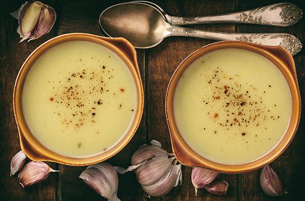 two ceramic bowls of soup, ivory colored garlic soup with seasoning on top