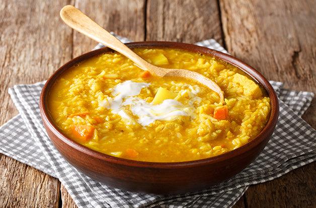 wooden bowl of soup, yellow soup with carrot and turkey chunks