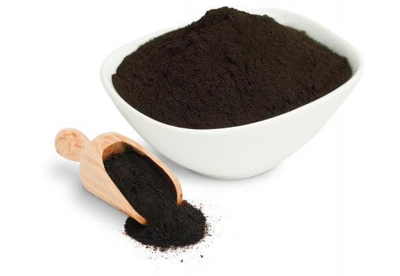blackish brown shilajit powder in a white bowl and wooden spoon