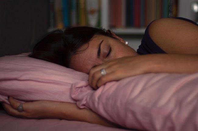 woman sleeping in her bed, pink sheets, dimmed lights. close up on face