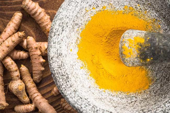 Tumeric powder in rustic bowl, turmeric root underneath