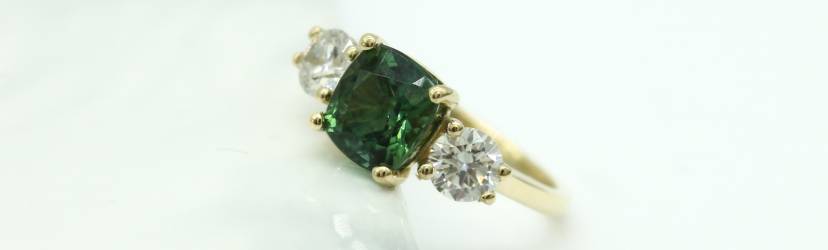 A custom gold engagement ring with a tourmaline, October's birthstone, set between two diamonds on a gold band.