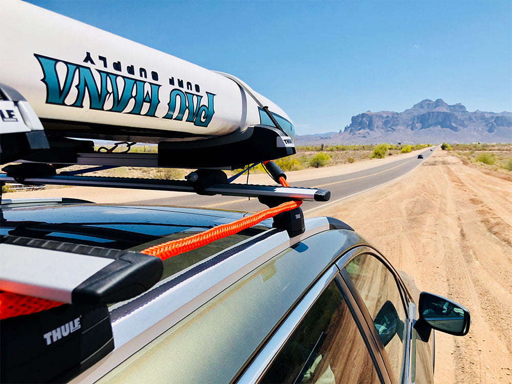 a paddlbaord onthe roof of a car driving down a scenic road