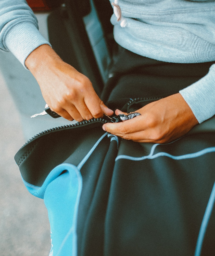 A person wearing a light blue jumper zipping a blue and black bag shut.