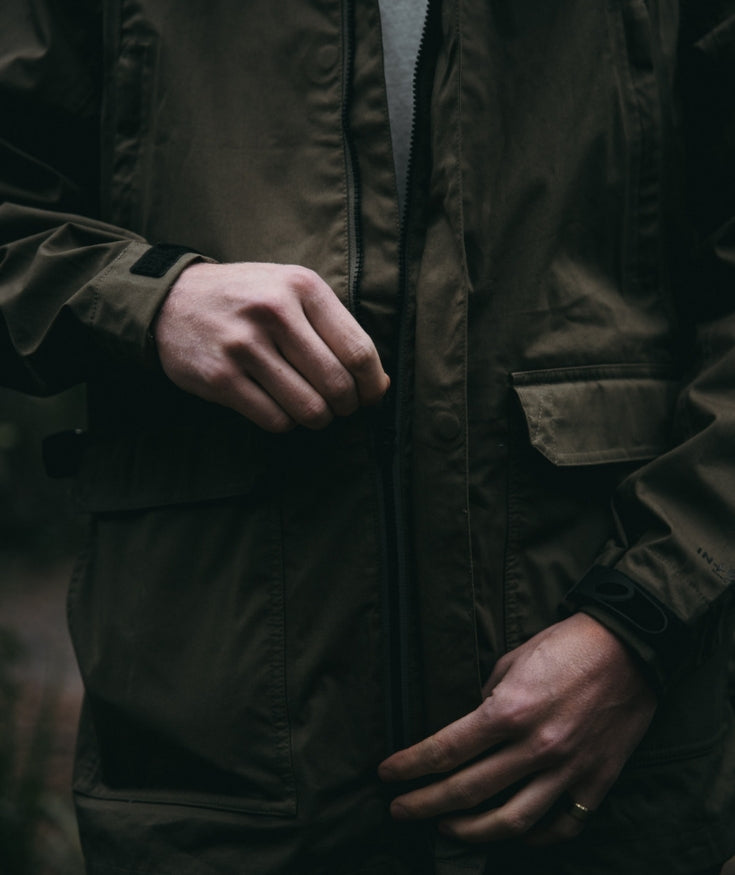 A man zipping a jacket zipper up to his chest.