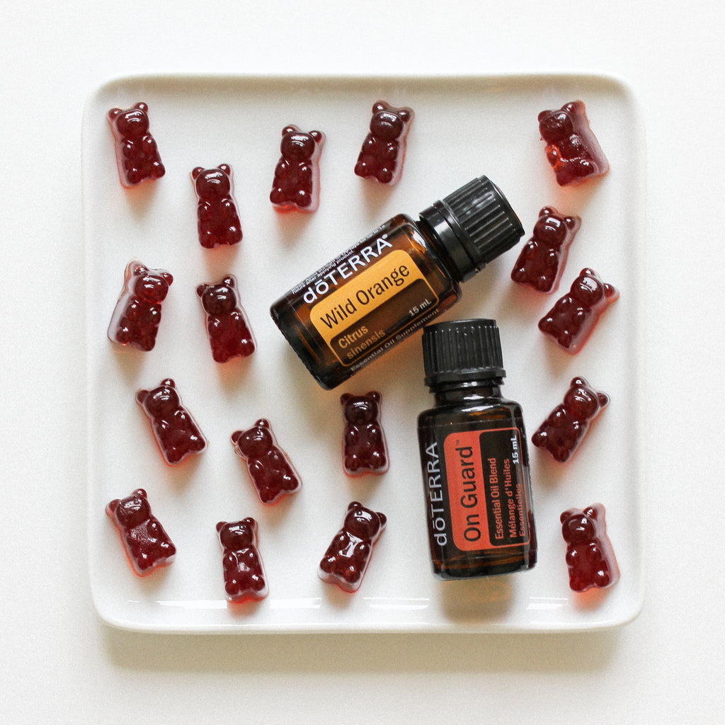 Pomegranate gummy bears surrounding a bottle of doTerra Wild Orange Essential Oil