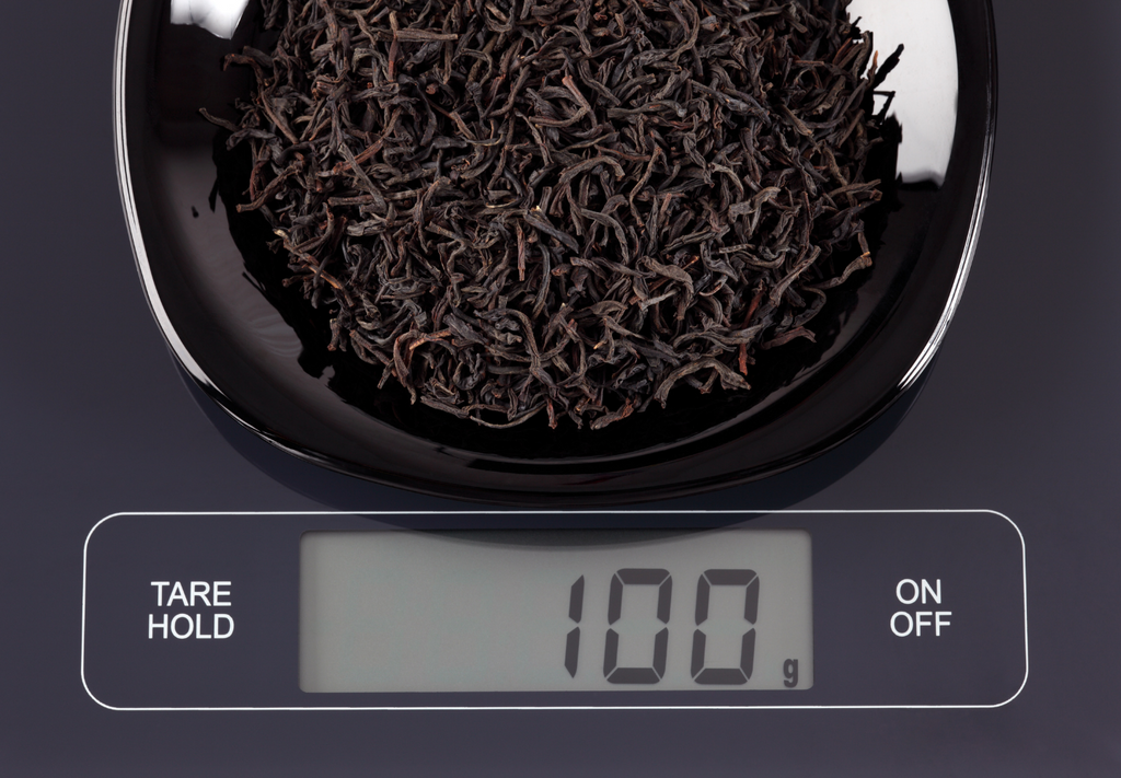 A set of digital scales with some black tea being weighed.