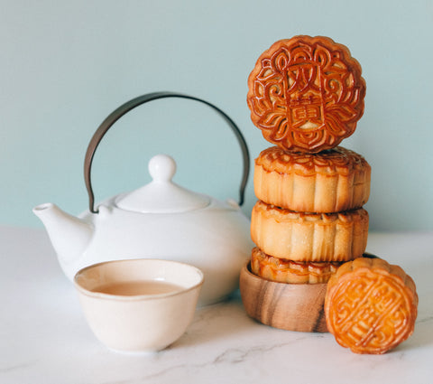 Stack of four mooncakes resting next to a white teapot and cup filled with a light tea