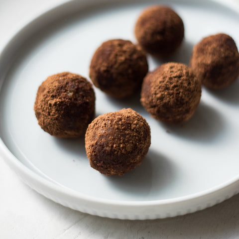 Six chocolate truffles sitting on a white plate against a white background