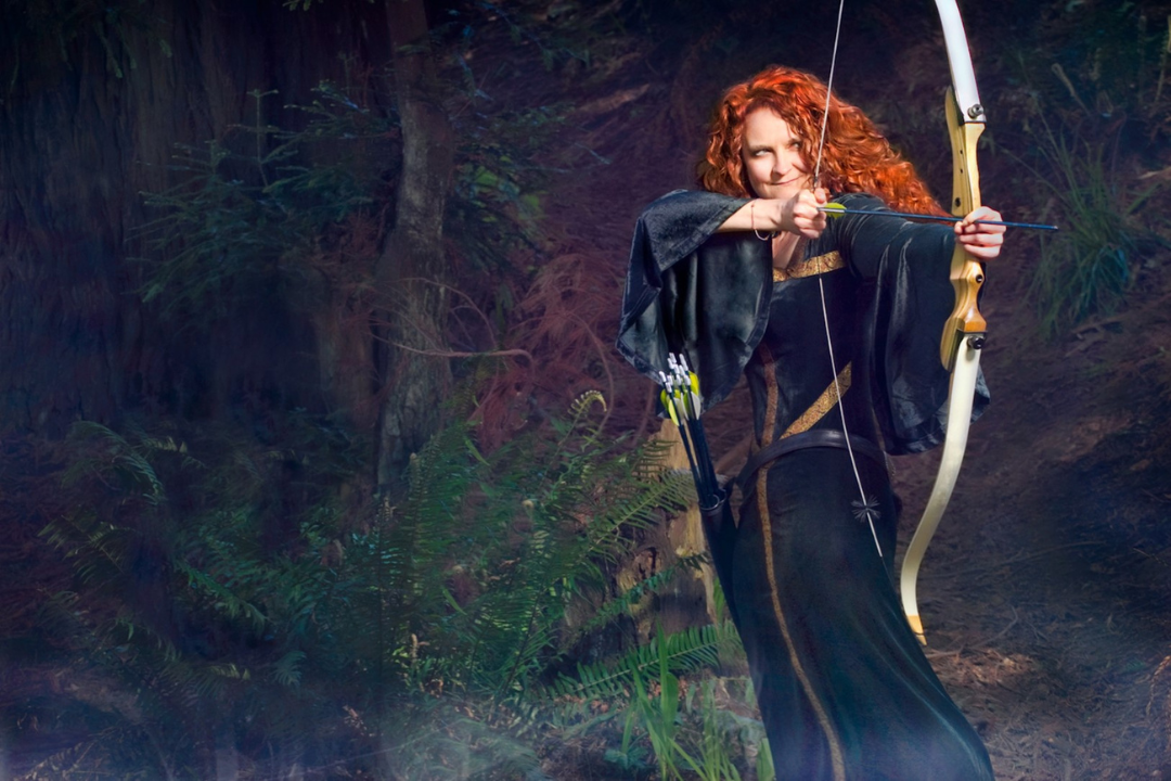 jessicurl founder, Jess McGuinty, dressed as Merida from Brave in a green dress and bow standing in a forrest