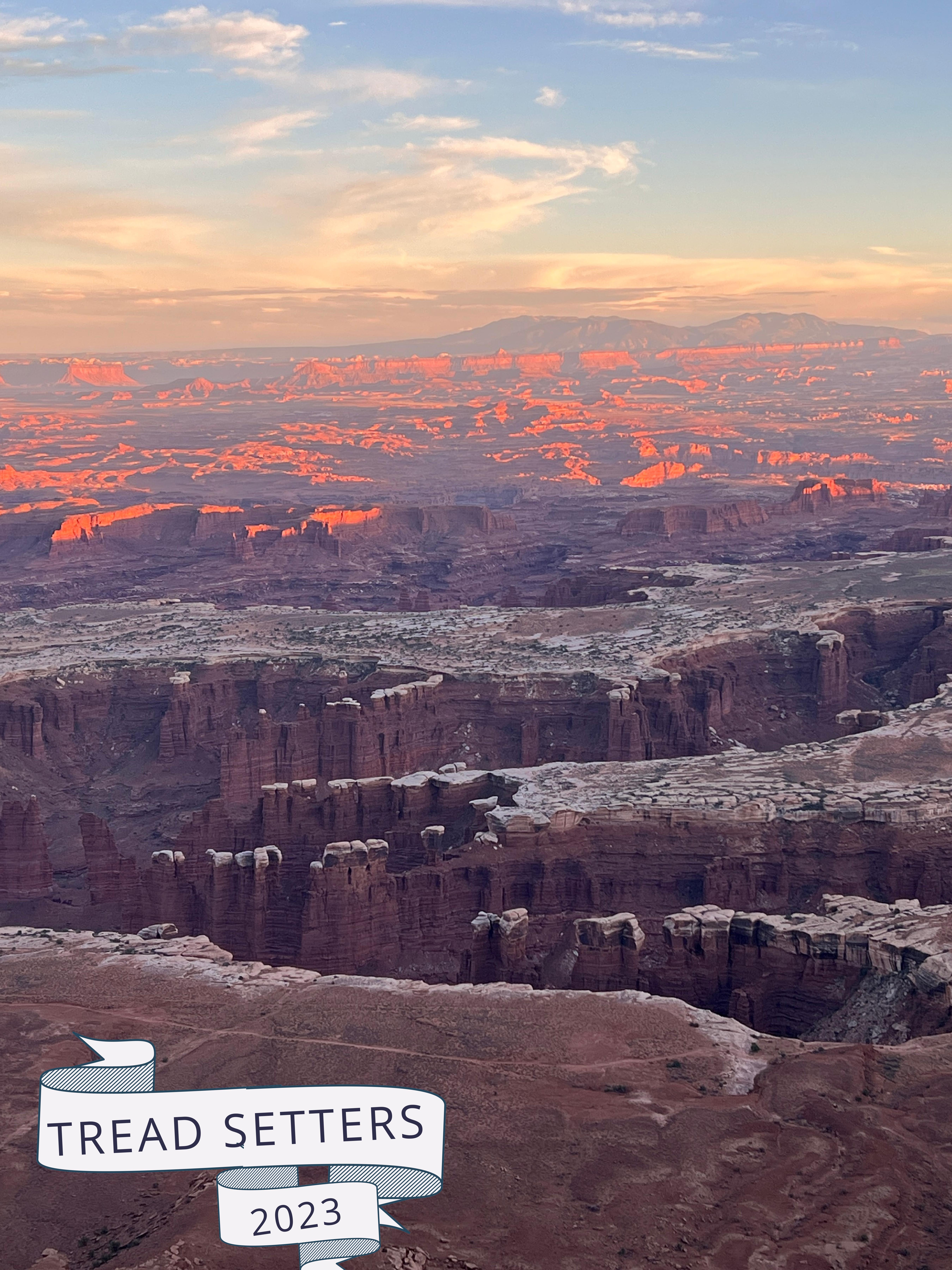 The sun lights up the depth of Canyonlands in the background while the canyons in the midground stand behind the shadow of a wall of canyons unseen. Upon scrutiny, there is a faint path, the White Rim Trail, that is relatively less impressive in the foreground, barely visible due to the details of the natural beauty in the background.  Credit: Dean Warren https://www.instagram.com/deanwarrenphotography/
