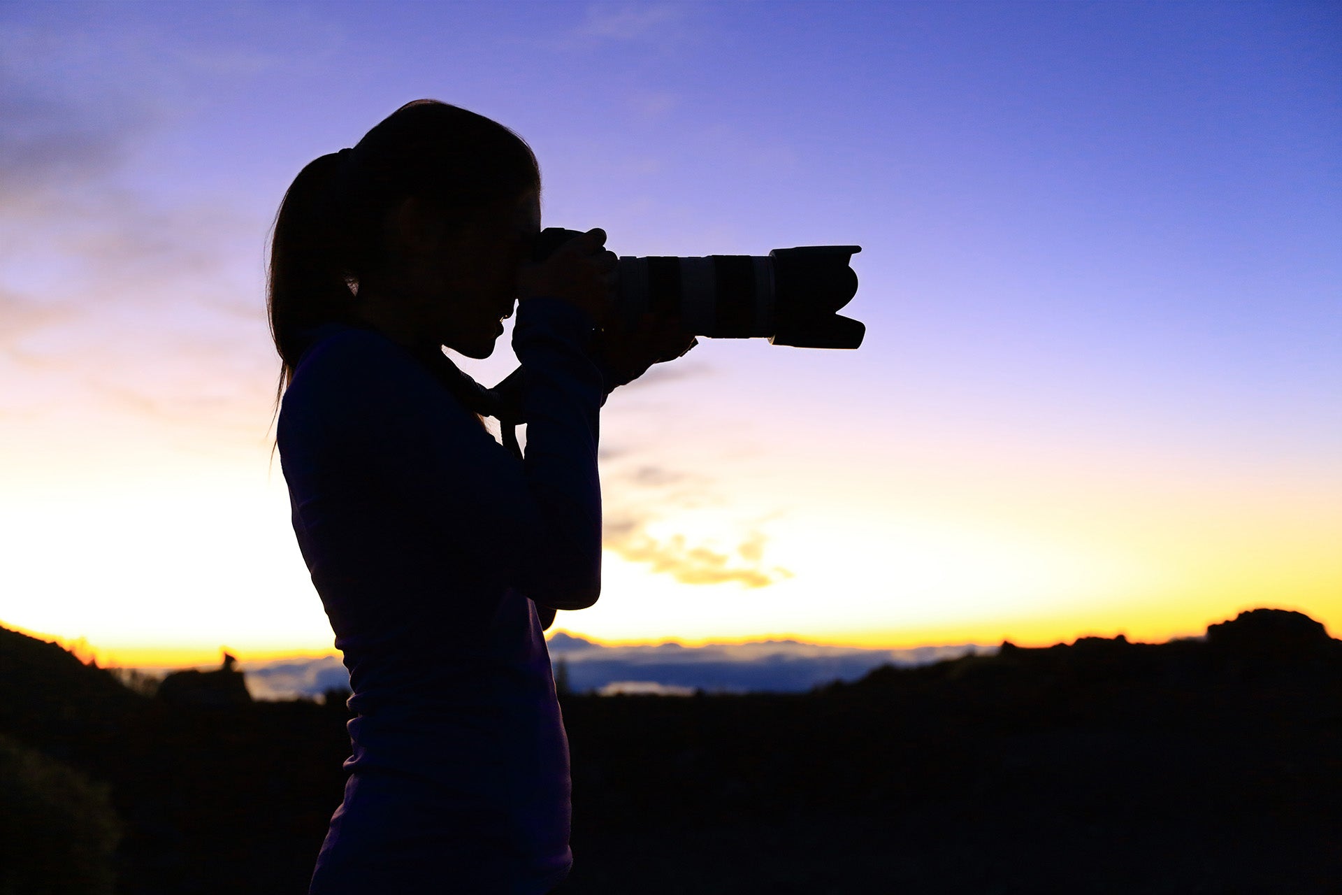 Mujer disparando con teleobjetivo al atardecer