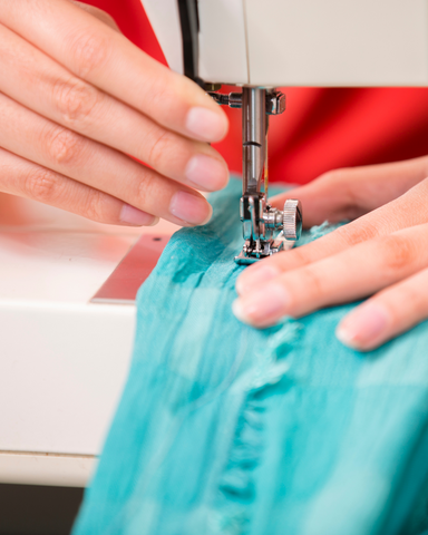 close up of two hands feeding fabric through a sewing machine.