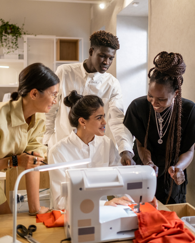 a diverse group of sewists talking around a sewing machine