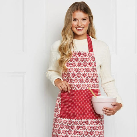 blond women in her 20s wearing a christmas apron and holding a mixing bowl