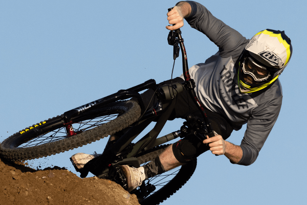 Cyclist in Troy Lee Designs D3 helmet riding at angle over dirt hill against blue sky