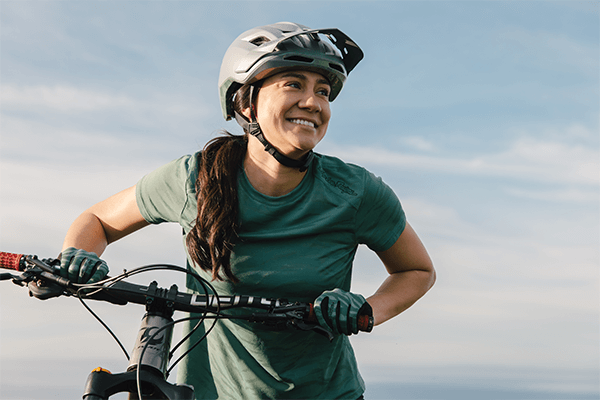 Female model smiling and wearing a TLD Flowline SE helmet holding bike against blue sky