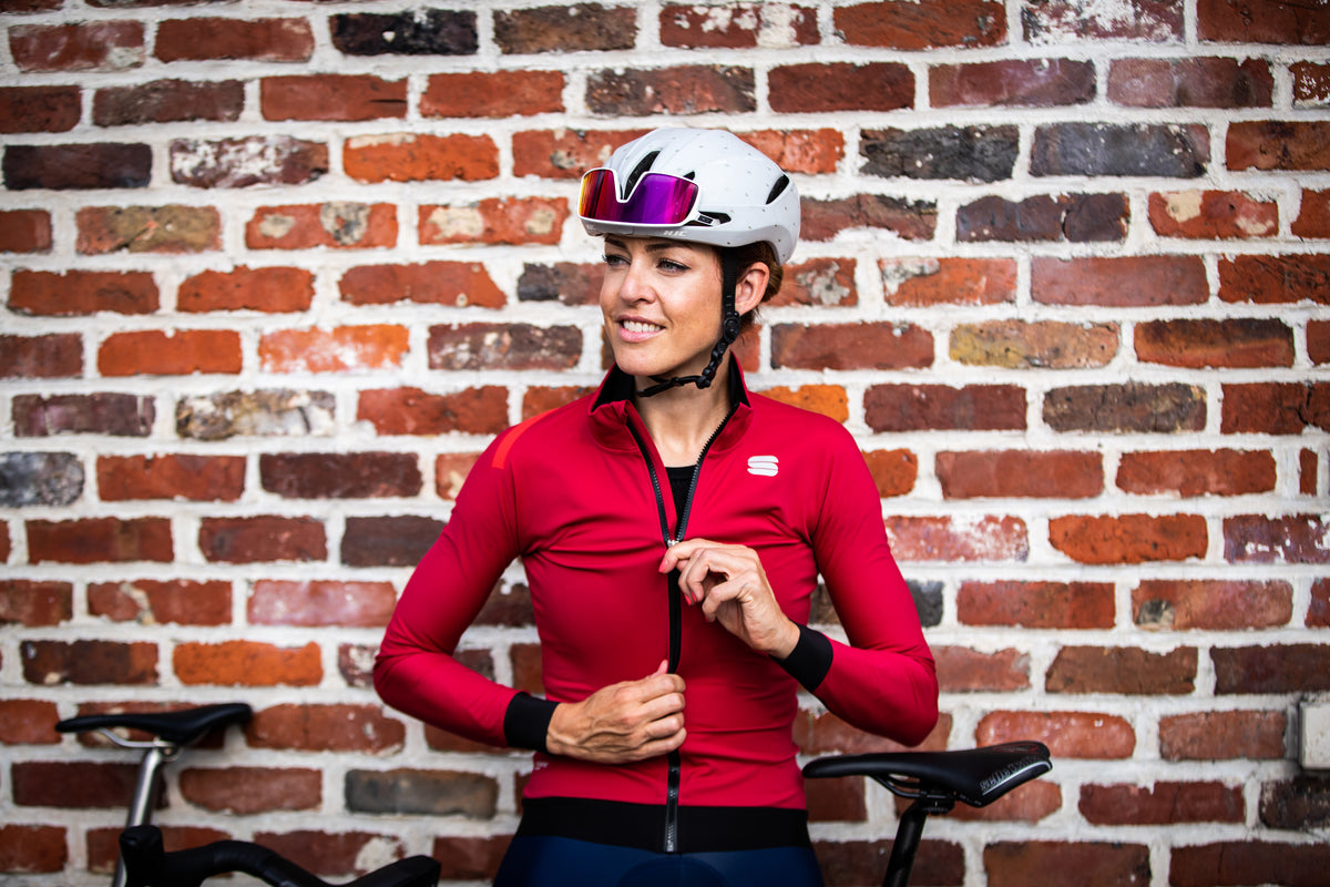 Female cyclists stands with back to wall to do up her Sportful Fiandre Pro Jacket