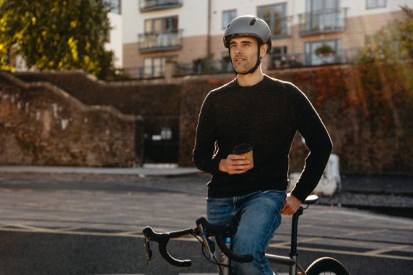Male model in a Calido Plus helmet standing over a bike seat holding coffee 