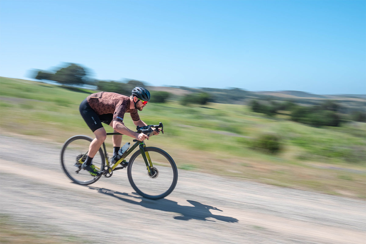 Man framed by blue sky riding gravel bike fast down slope