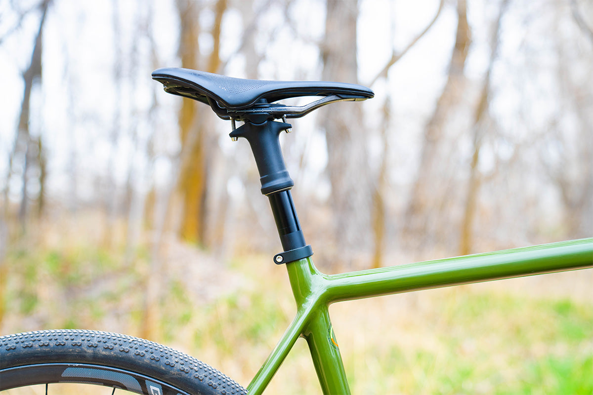 A close up of a black ENVE dropper post on a green bike in a wood