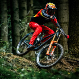 Male cyclist riding through forest in Race Red Troy Lee Designs Skyline Sprint Trousers