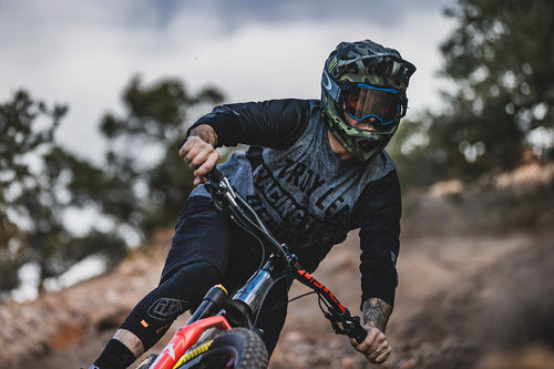 Cyclist riding a mountain bike wearing the Troy Lee Designs Ruckus Jersey in grey and the Troy Lee Designs Stage helmet in camo