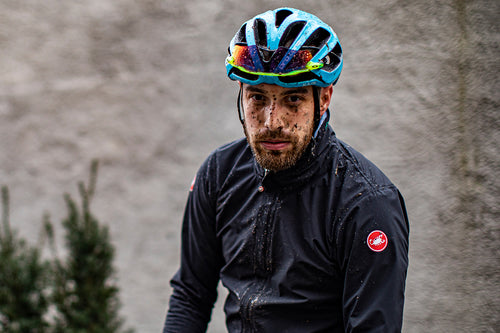 Photo of a cyclist looking at the camera semi side on wearing the Castelli Gavia Rain Jacket speckled in mud