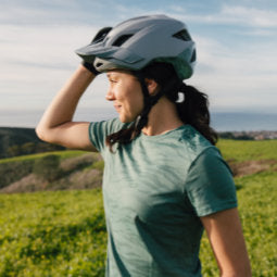 Female cyclist in green top standing looking out over green hills wearing a Troy Lee Designs Flowline SE Helmet