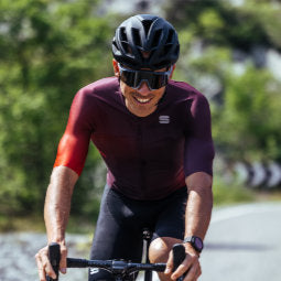 Smiling male cyclist riding along a tree lined road wearing a huckleberry Sportful Light Pro jersey