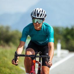 Female cyclist riding on road with mountains in background wearing a  jersey