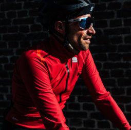 Male cyclist framed against a brick wall wearing a red Sportful Fiandre Pro jacket