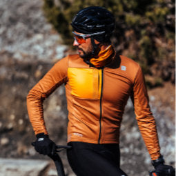 Male cyclist looking behind him on stationary bike wearing burnt orange Sportful Super Jacket