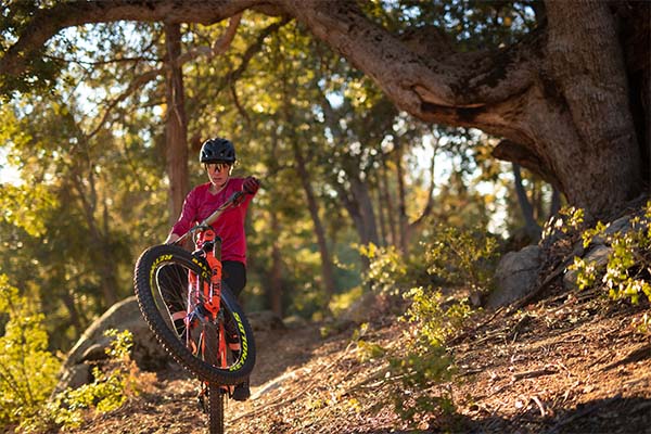 Female cyclist lifting off in sunny woods in TLD Mischief kit