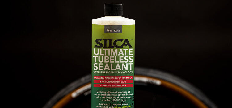 Studio shot of SIlca Ultimate Tubeless Sealant against a black background with the top of a wheel visible behind