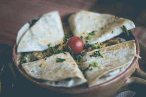  quesadilla on plate topped with chives and a cherry tomato