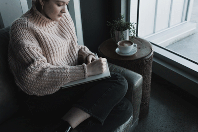 woman journaling on sofa beside cup of coffee