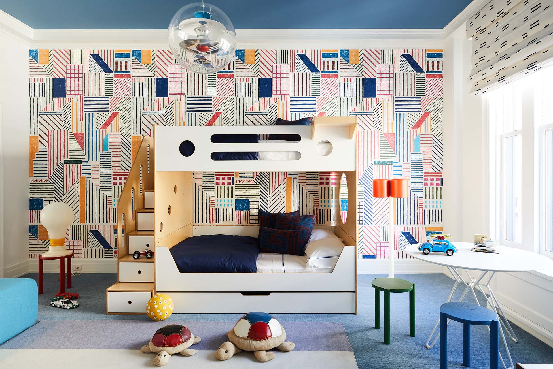 Modern children's room with geometric wallpaper, white bunk bed, and playful seating areas.