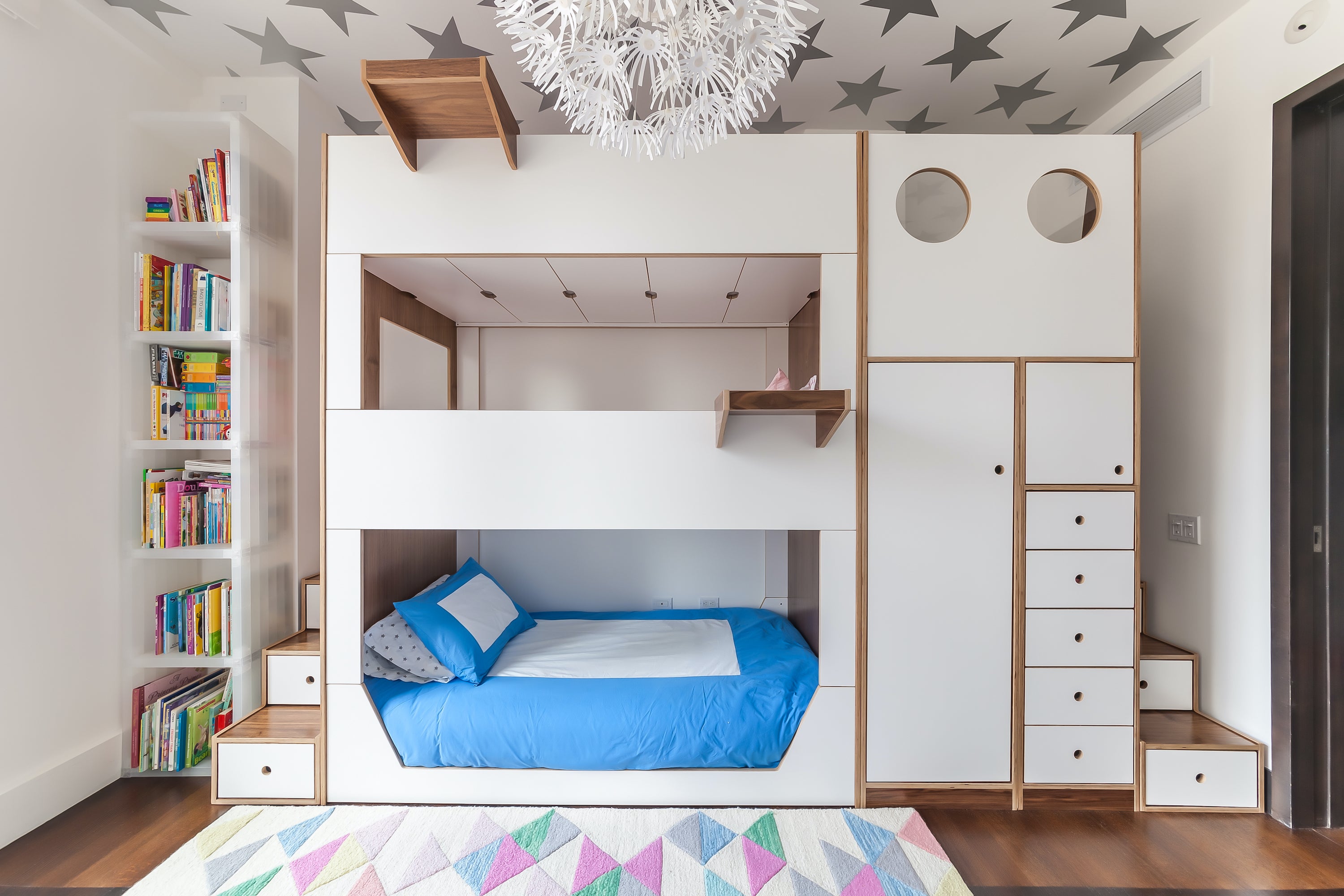 A stylish child's bedroom featuring a white bunk bed with blue bedding, and a ceiling adorned with star patterns.