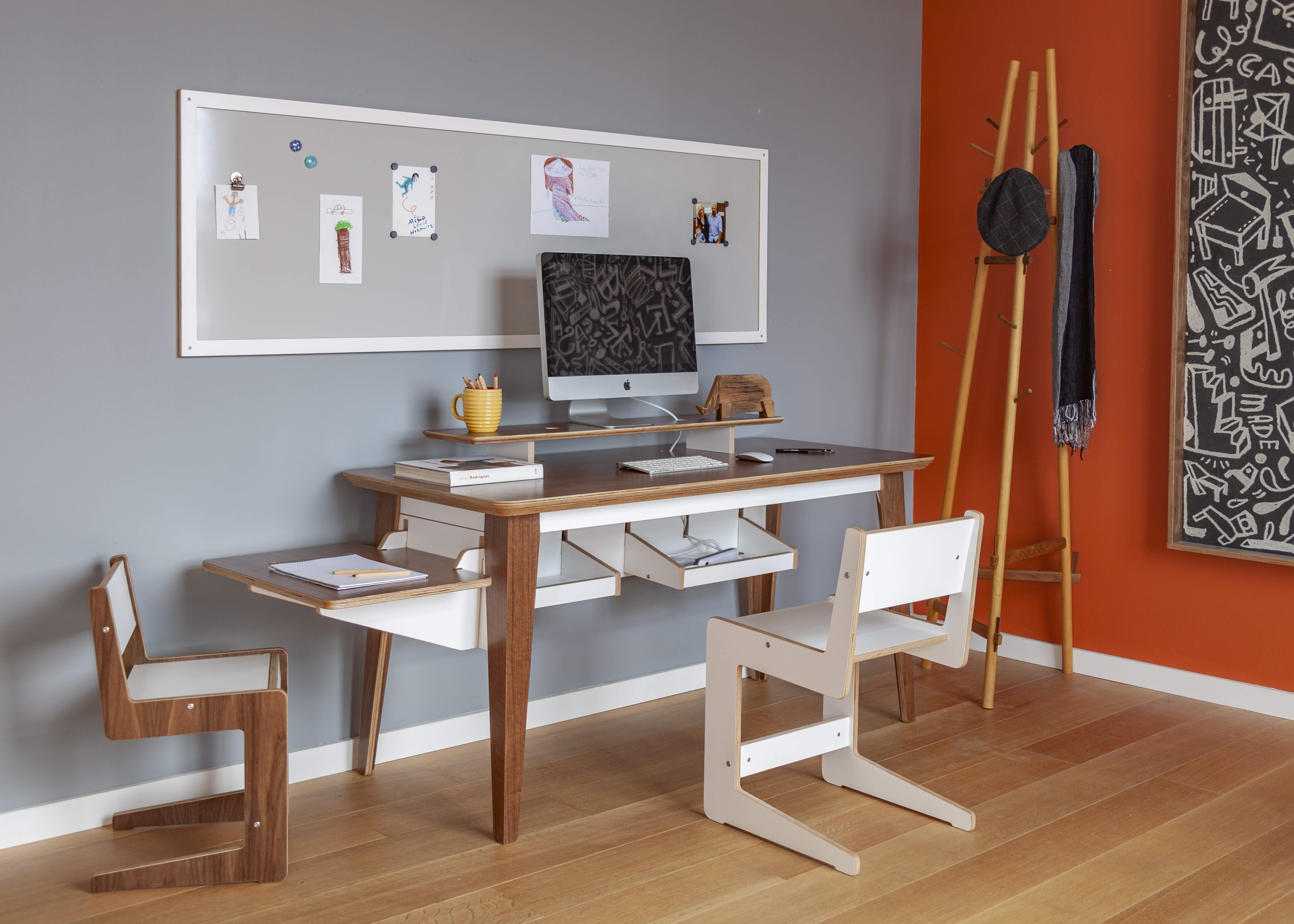 Modern home office with desk, computer, chairs, and artwork.