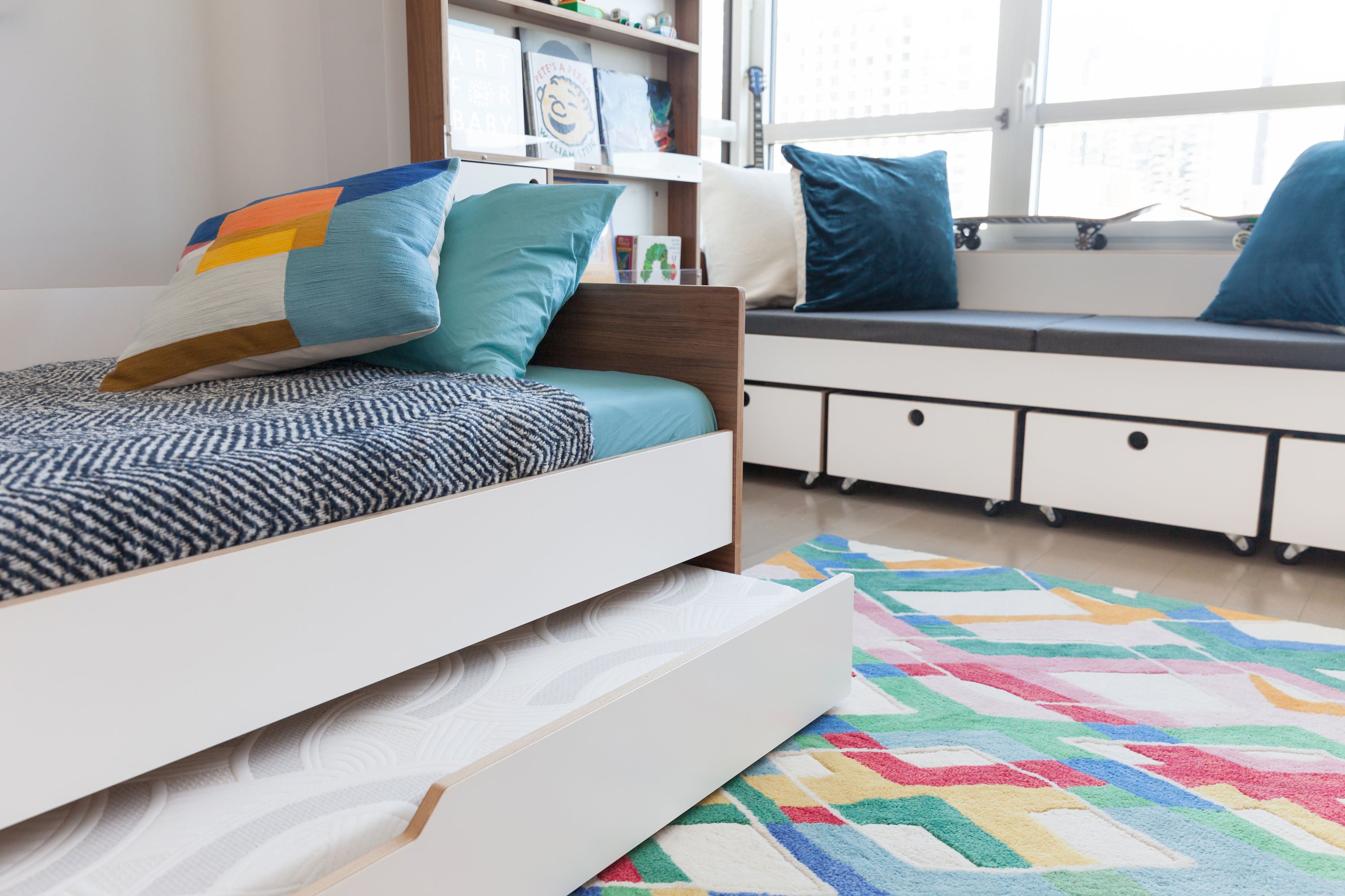 Bedroom with colorful rug, bed, drawers, daybed by window.