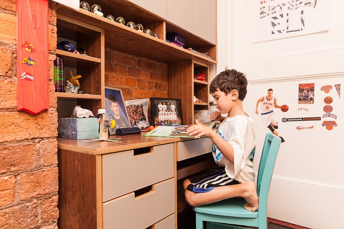 Child at desk with books, sports memorabilia, and photos.