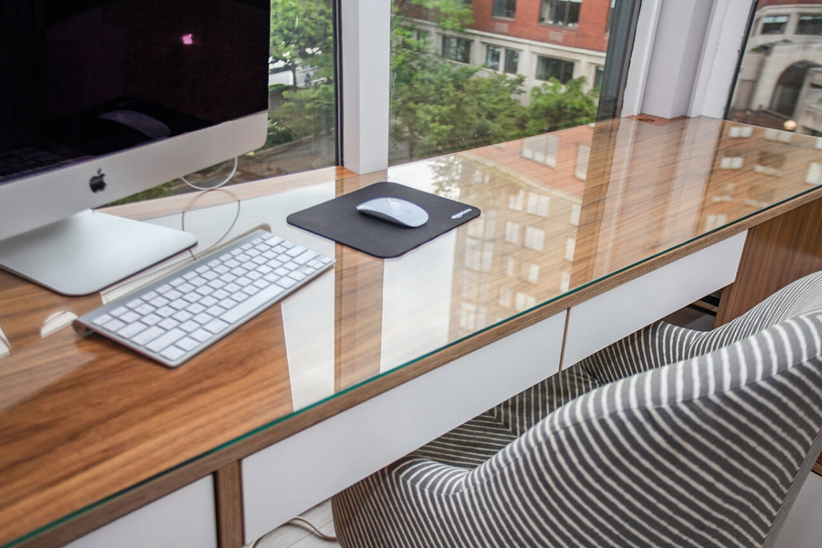 Desk with iMac, keyboard, mousepad, and mouse by window overlooking trees.