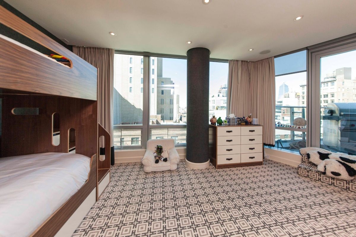 Spacious bedroom with large windows, bunk bed, and patterned carpet in an urban setting.