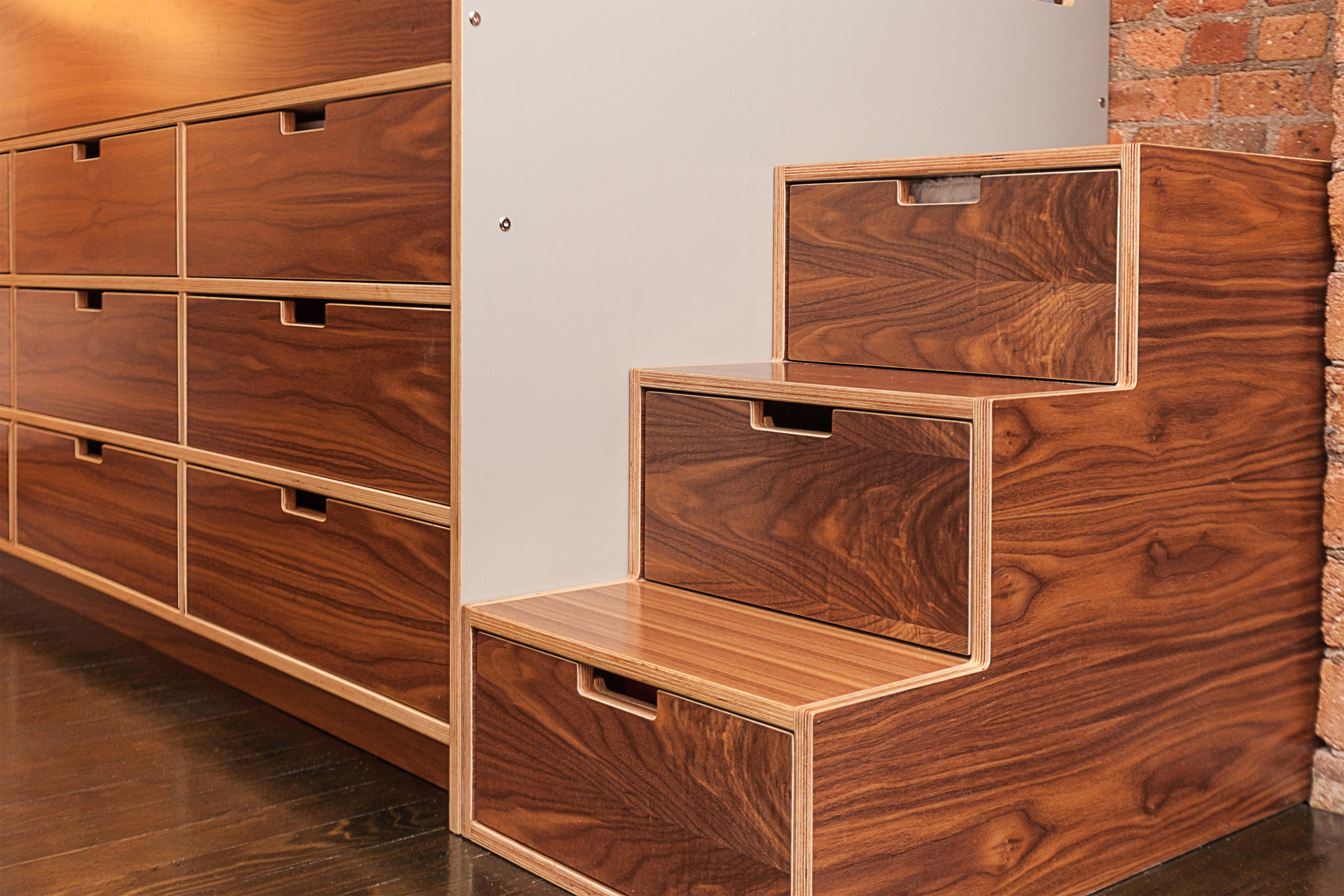 Custom wooden storage drawers with unique pull-out steps against a brick wall, elegant and functional.