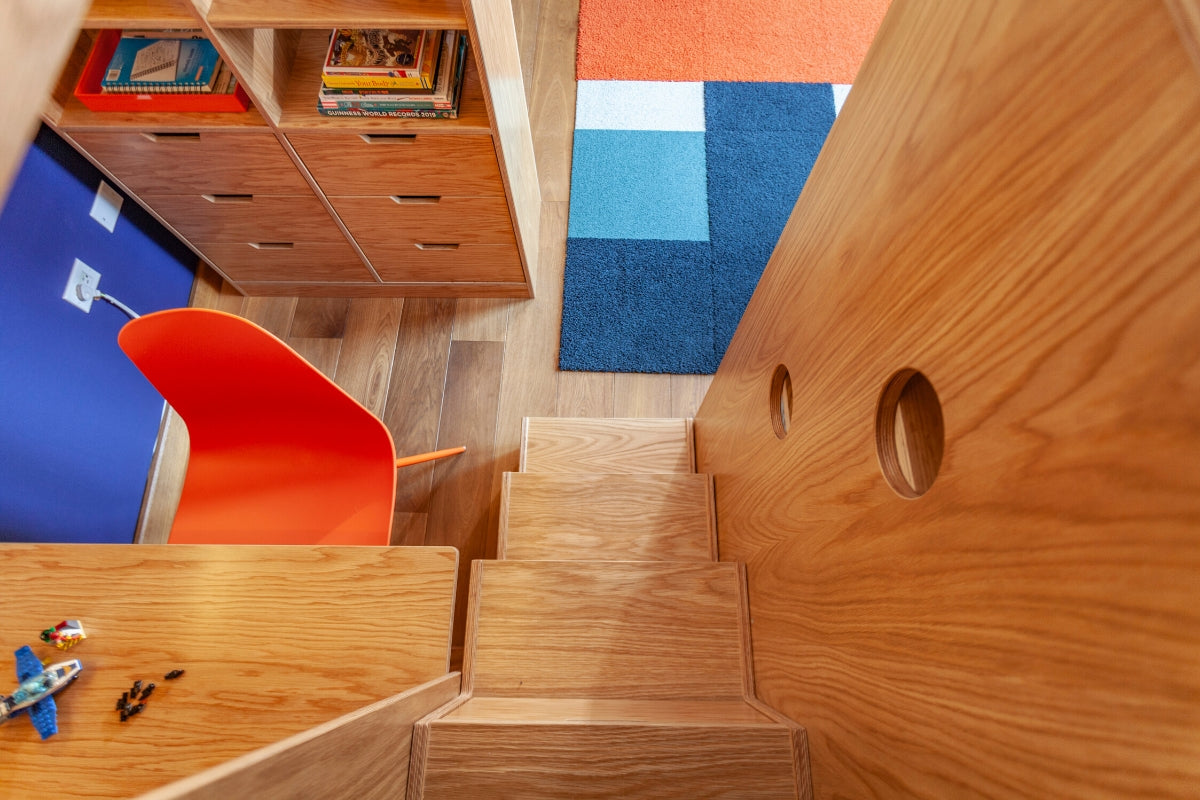 Wooden loft bed with storage, study space, and colorful rug.