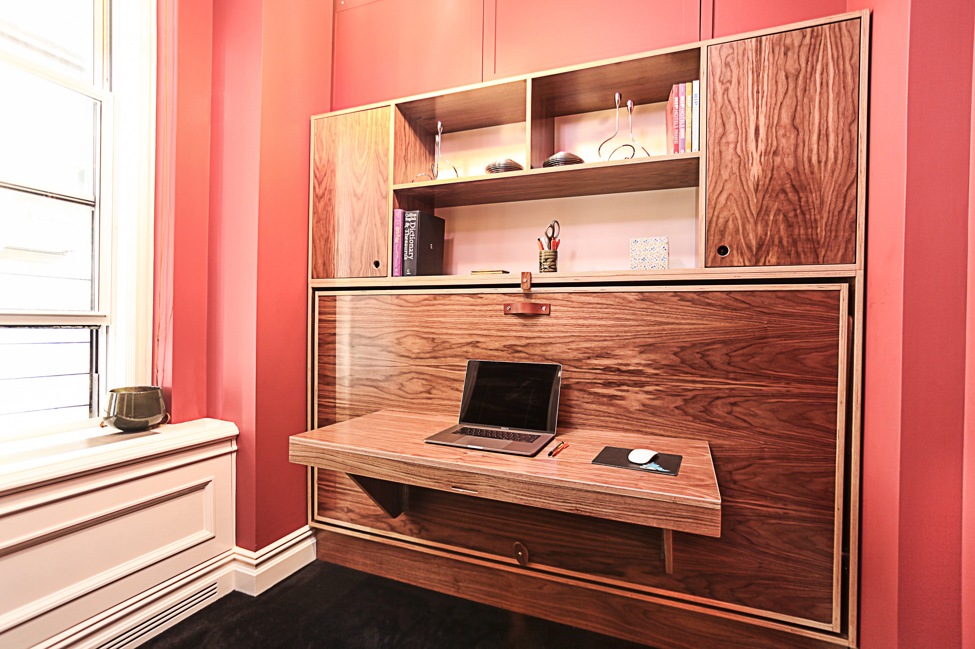 Compact workspace with a fold-down desk from a murphy bed unit, in a room with red walls.