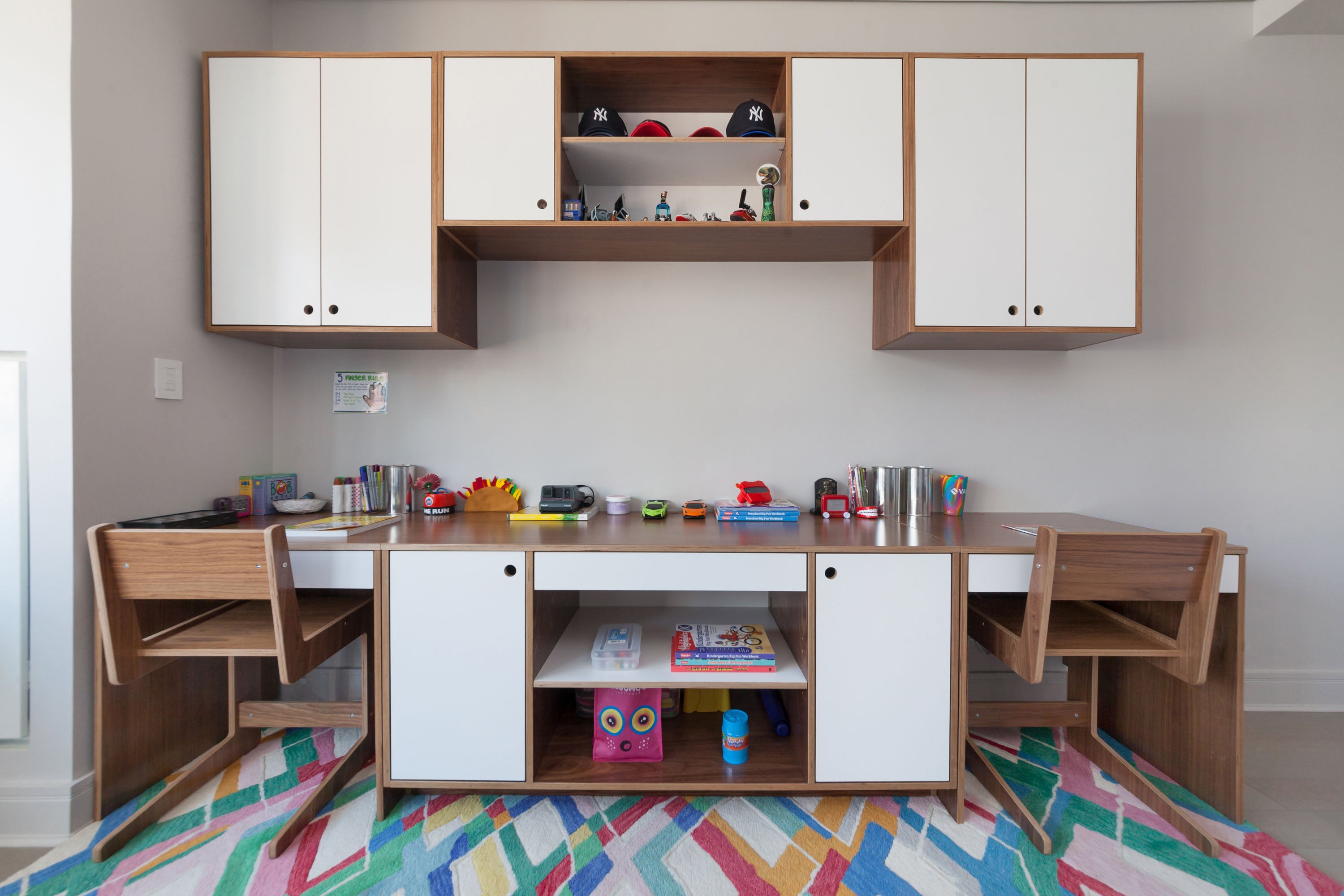 Kids’ study space with wooden desk, cabinets, colorful rug, and toys.