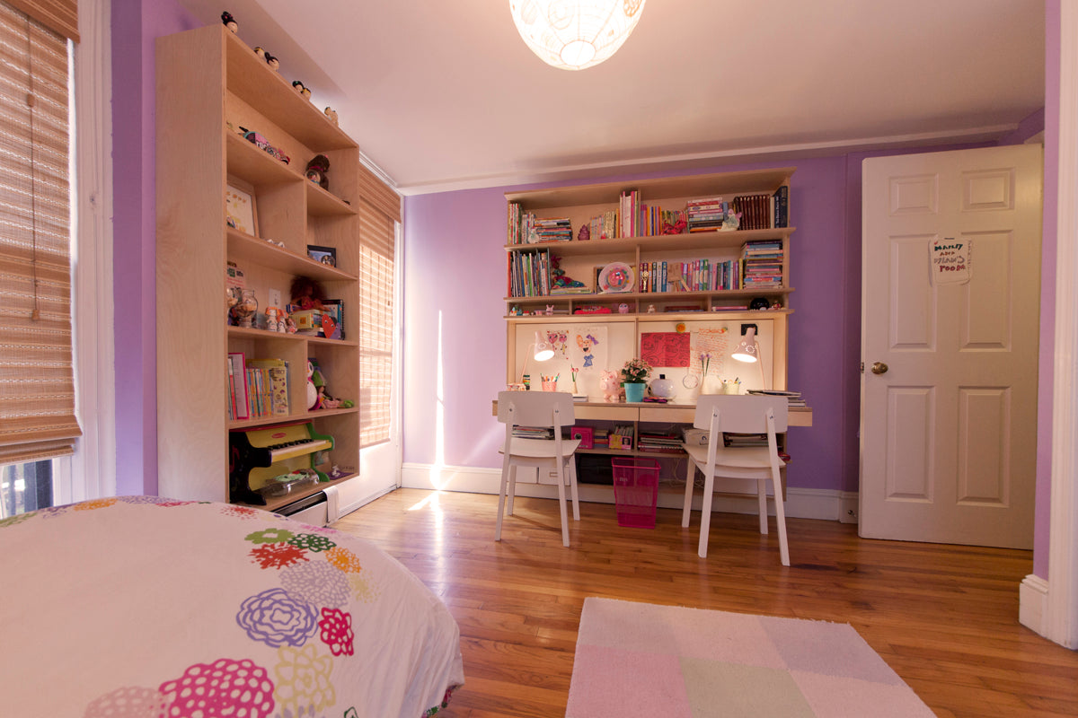 Cozy child's study area with desk, chairs, bookshelves, and a large overhead light in a purple room.