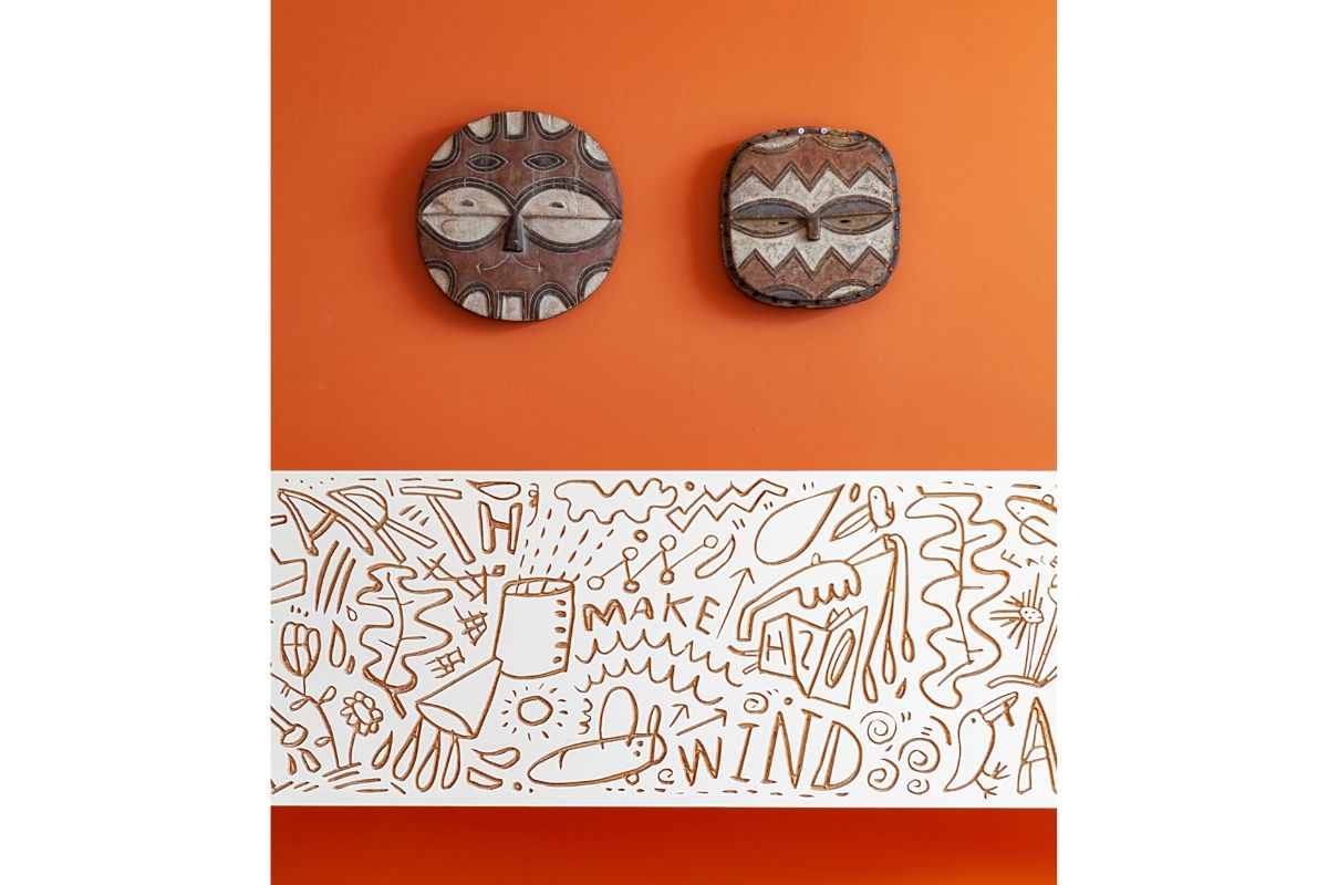 Tribal masks, doodle art, “MAKE WINDS” on orange wall.